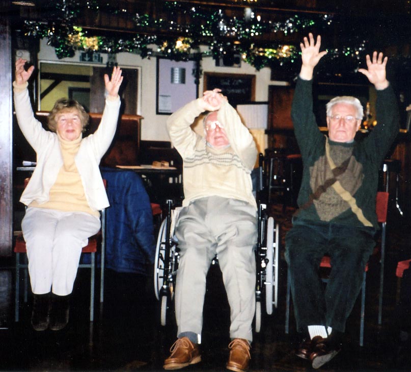 Three older people raising their arms during a seated activity